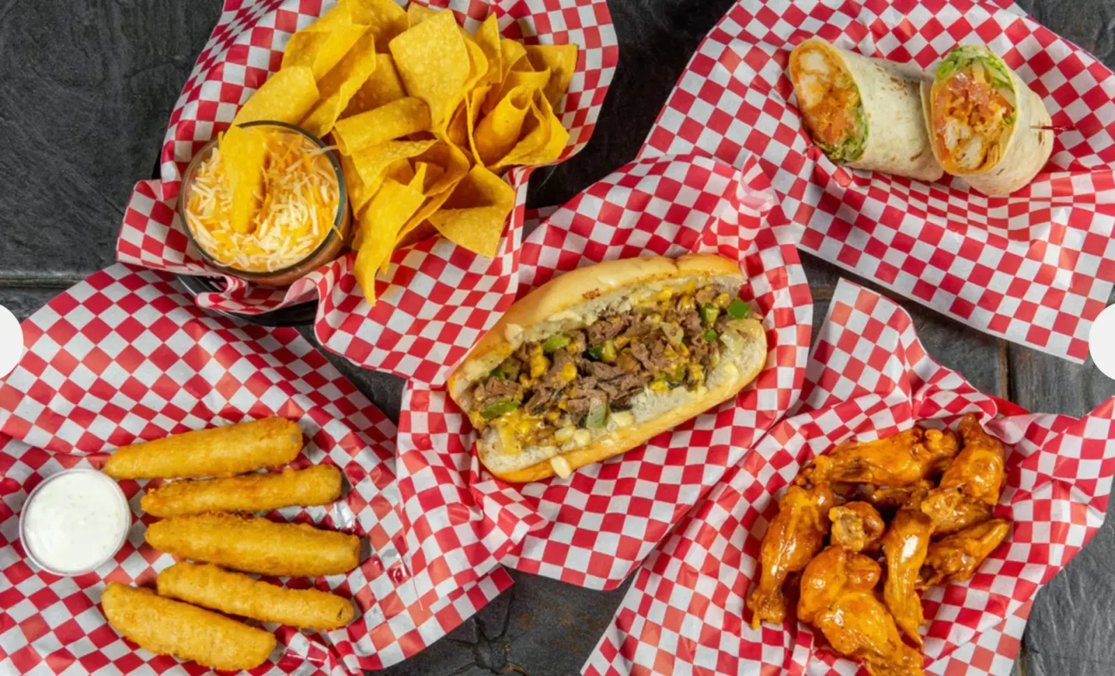 Scorers wings, a cheesesteak, mozzarella sticks, a buffalo chicken wrap, chips, and queso in red-and-white baskets
